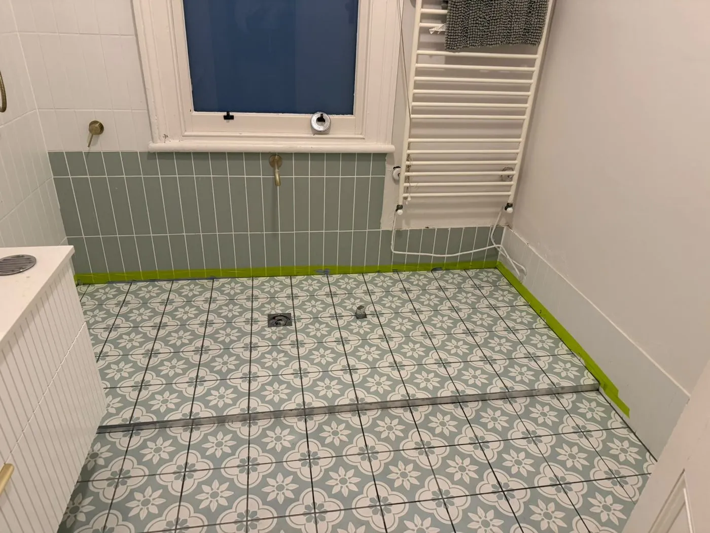 Patterned floor tiles and sage-green wall tiles in a renovated bathroom
